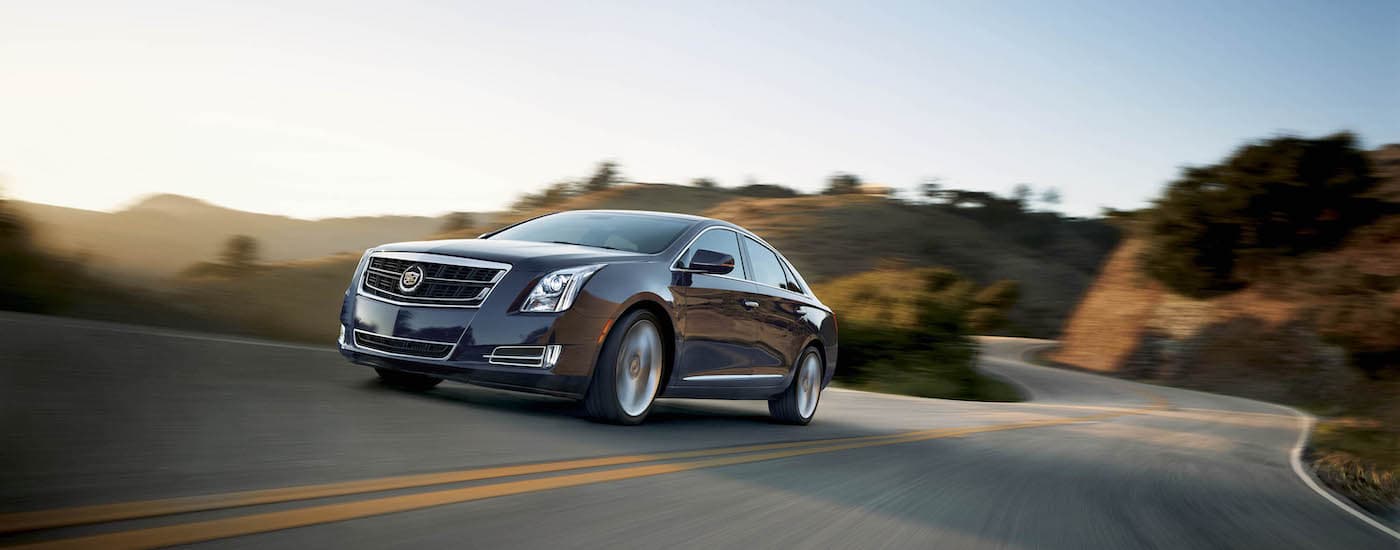 A grey 2015 Cadillac XTS, popular among used luxury cars in Fort Worth, TX, is driving on a sunny road.
