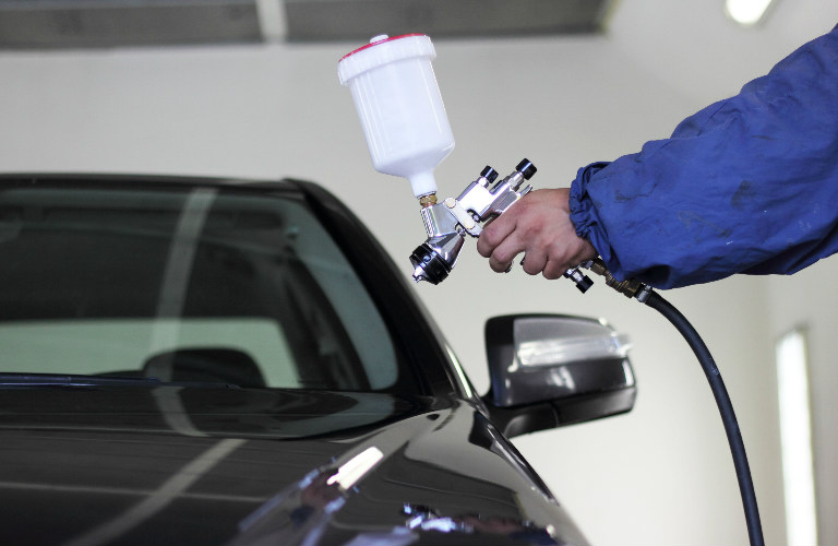 service technician aiming spray paint gun at car