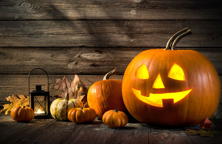Jack-o-lantern and other pumpkins and a lantern lined up on a wood floor and background